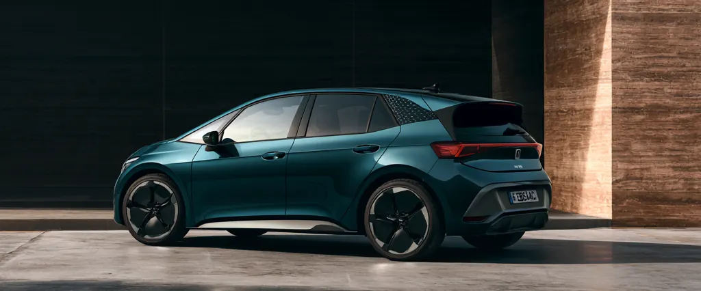 Carro eléctrico teal estacionado bajo una losa de concreto, junto a un muro de tierra apisonada